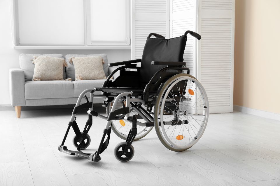 Wheelchair in a room, with a couch in the background. White walls, wooden floor.