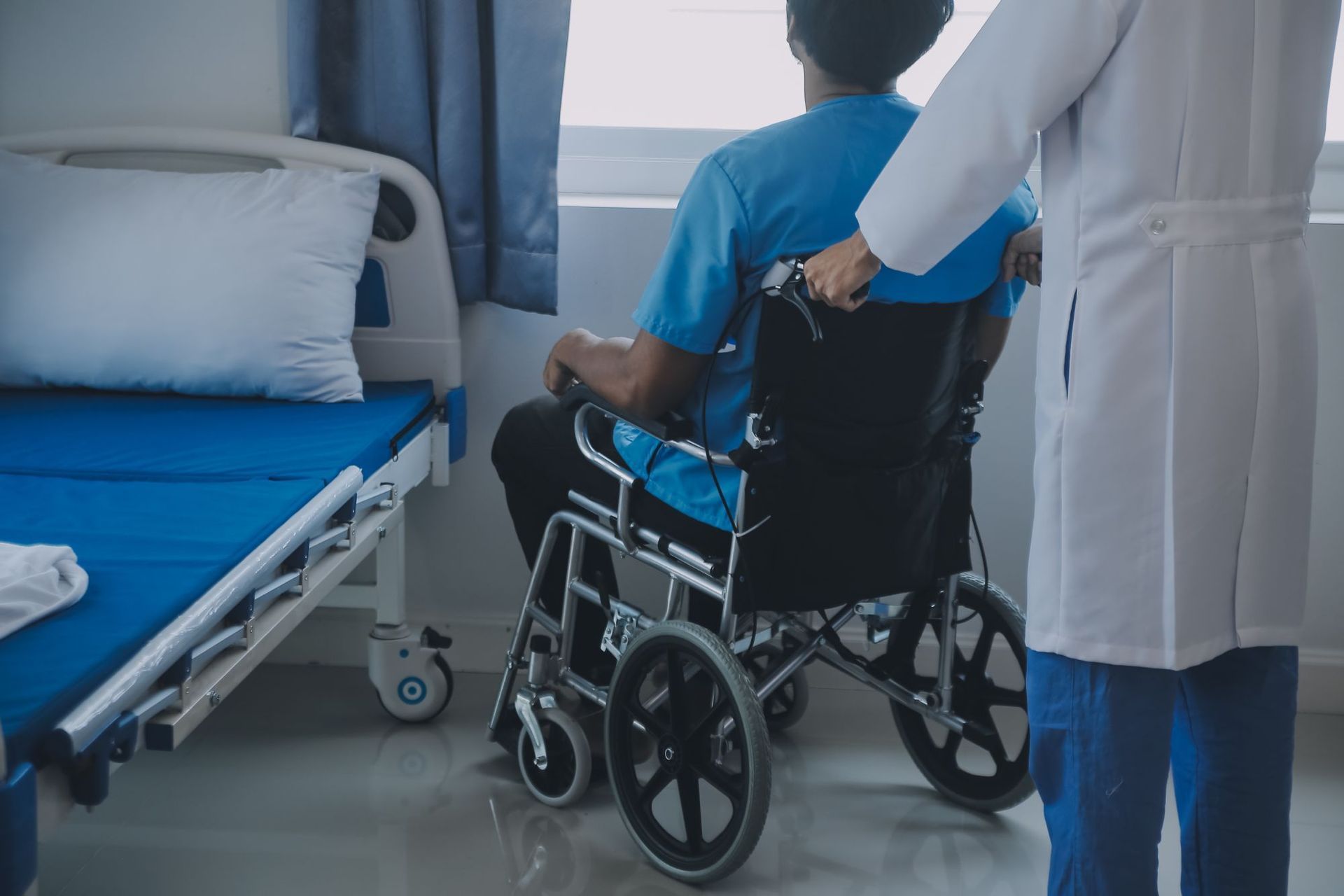 Person in wheelchair assisted by a doctor in a hospital room.