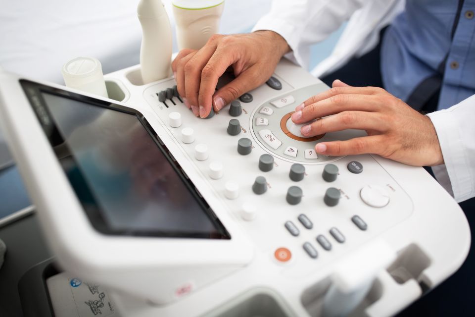 Hands operating an ultrasound machine, adjusting dials and controls on the console.