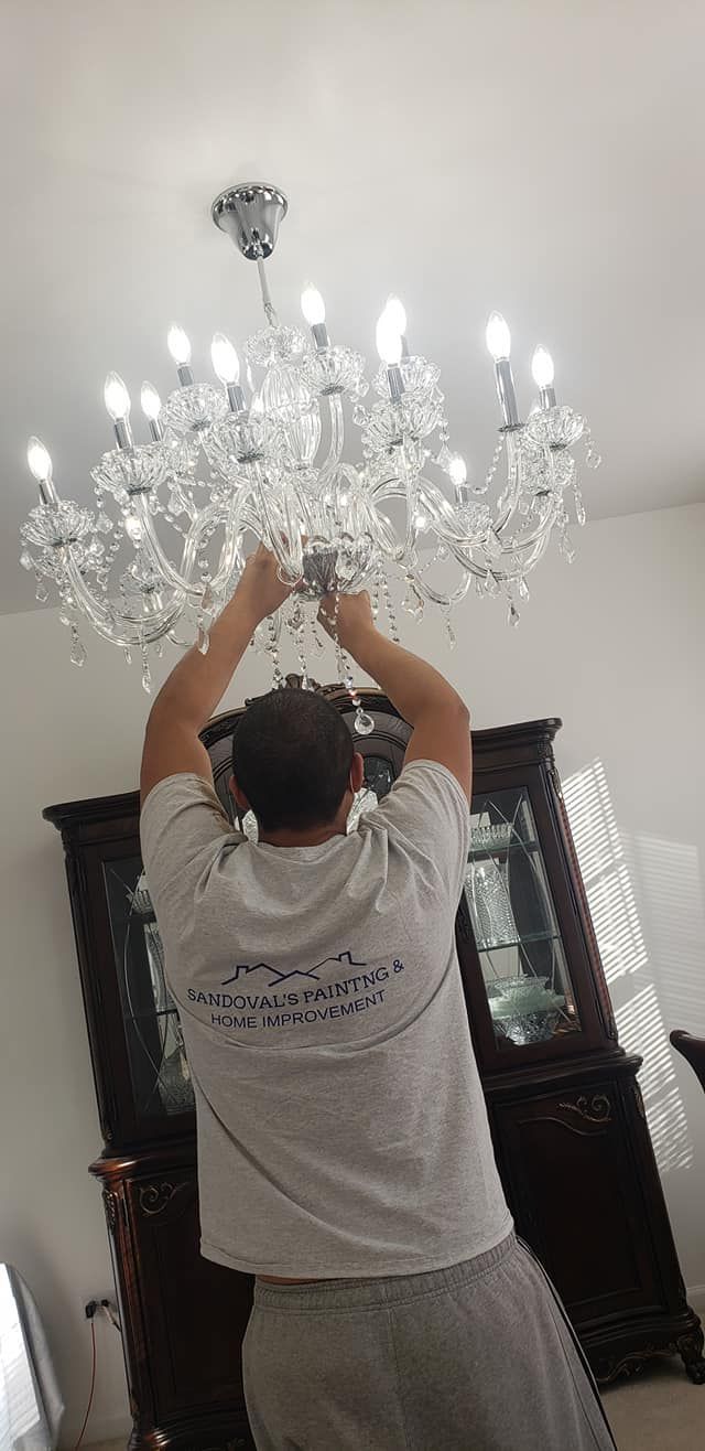Person adjusting a crystal chandelier in a room with dark cabinets and white walls
