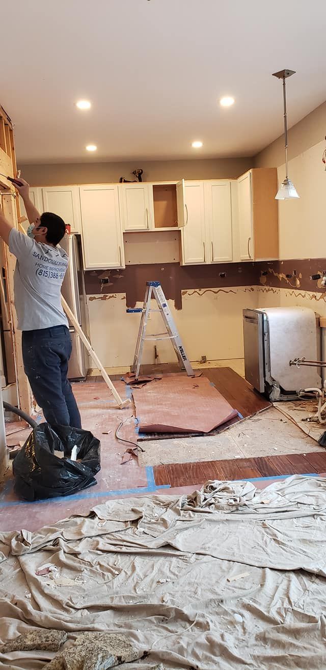 Kitchen under renovation with tools, debris, and a worker painting near a ladder
