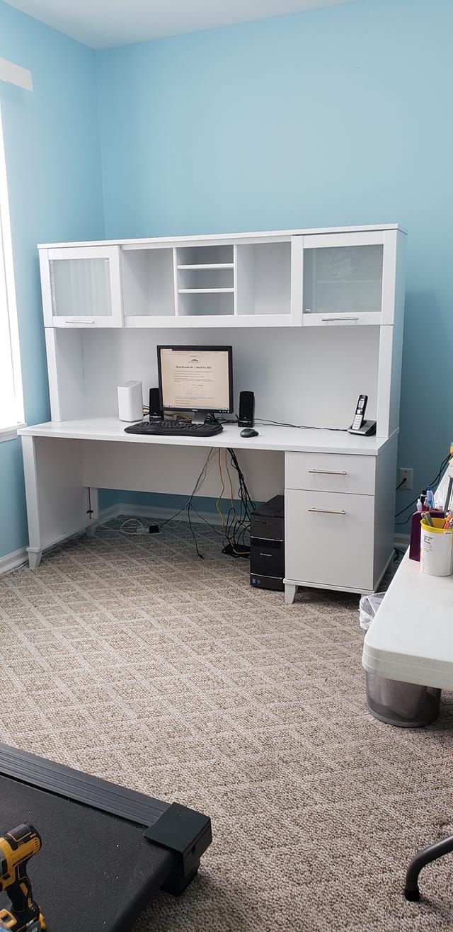 White desk with shelves and computer in a light blue room with carpeted floor