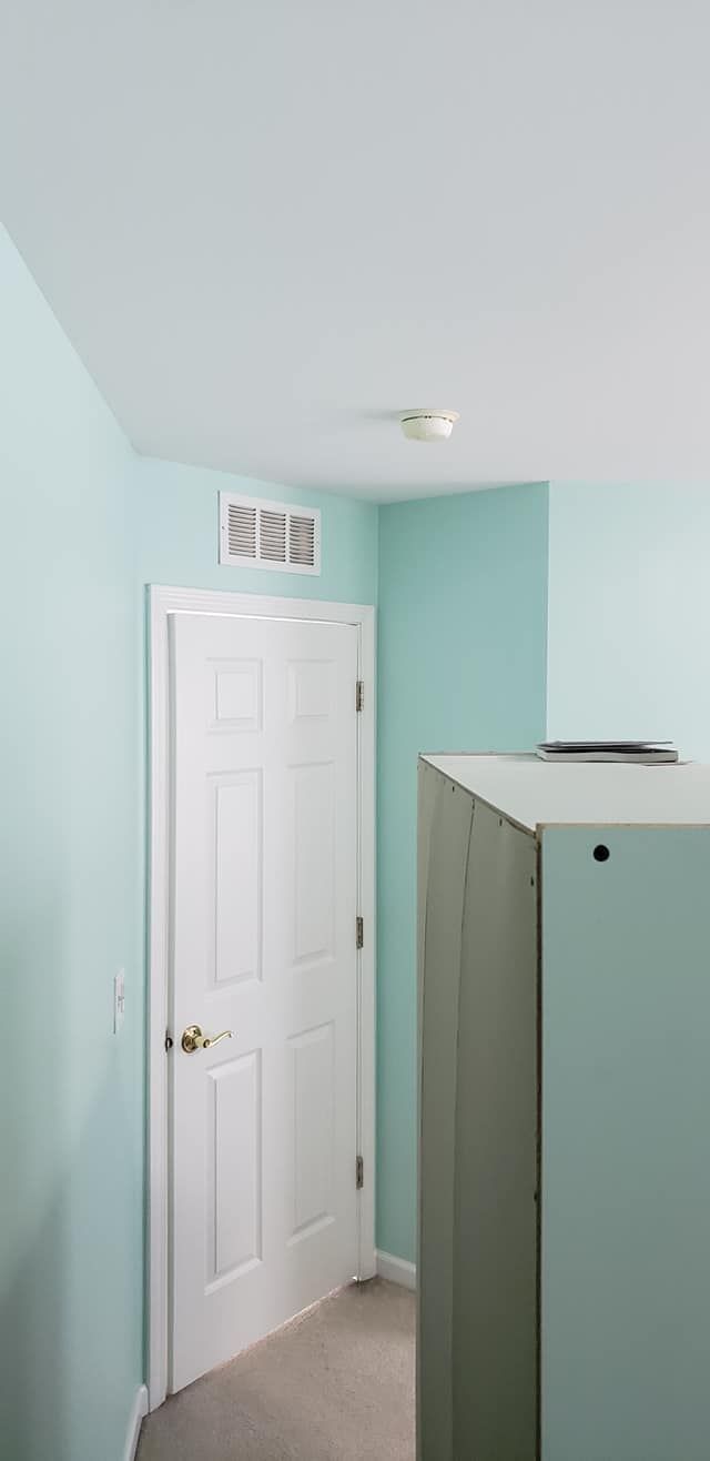 Small pale-blue hallway with a white door and a light gray cabinet under a ceiling light.
