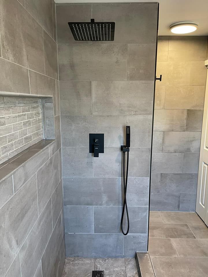 Modern tiled walk-in shower with rainfall head, handheld wand, and recessed shelf.