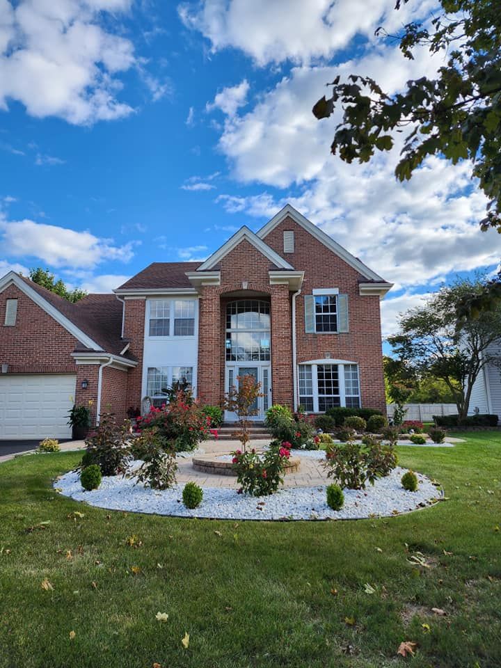 Brick suburban house with white-trimmed windows, landscaped front yard, and blue sky with clouds