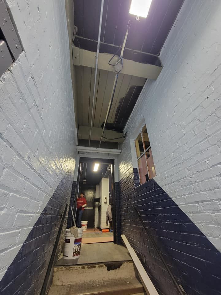 Narrow indoor stairwell with blue and white walls, exposed ceiling pipes, and a person near the bottom step