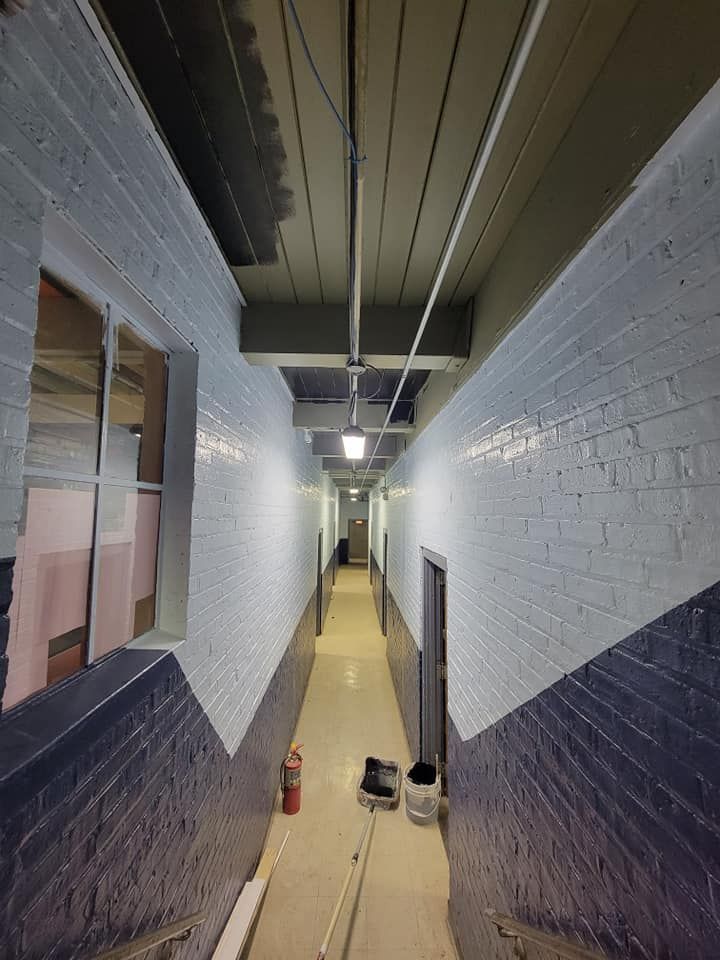 Narrow hallway with white brick walls, exposed ceiling, and tools on the floor during renovation.
