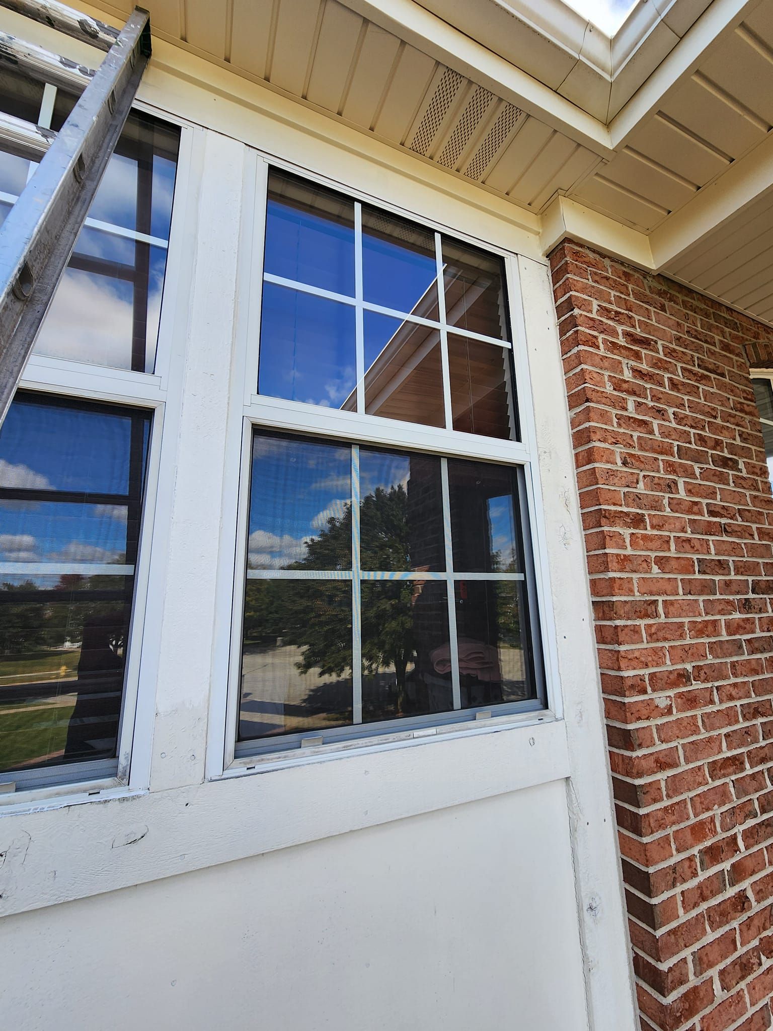 White-trimmed window beside red brick wall under a porch roof with blue sky reflections