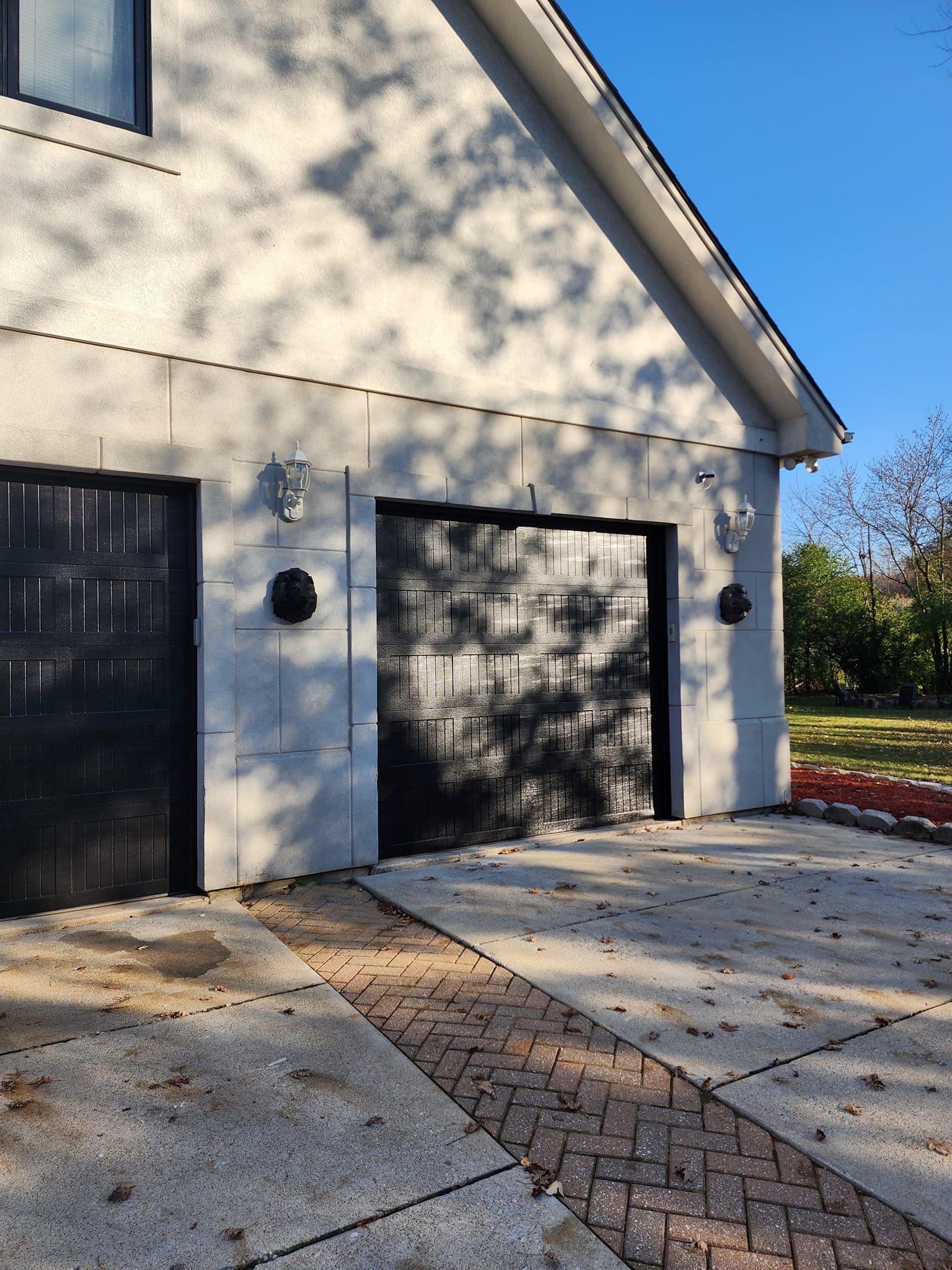 White stucco garage with dark doors and sunlit concrete driveway beside a landscaped yard.