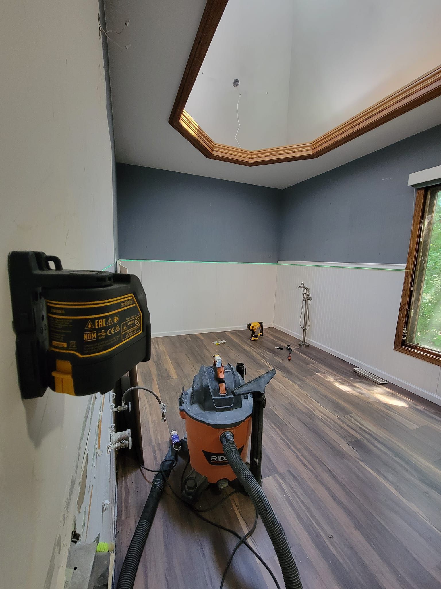 Vacuum cleaner in an empty room with gray walls, wood floor, and ceiling lighting.