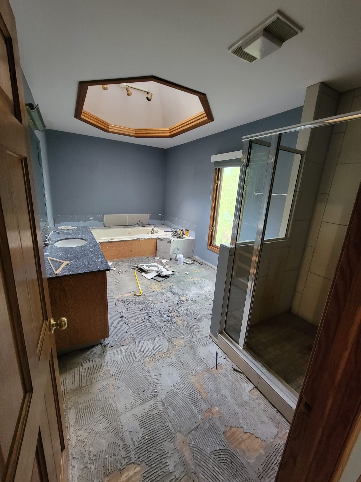 Cluttered bathroom under renovation with gray walls, vanity, tiled floor, and open shower stall
