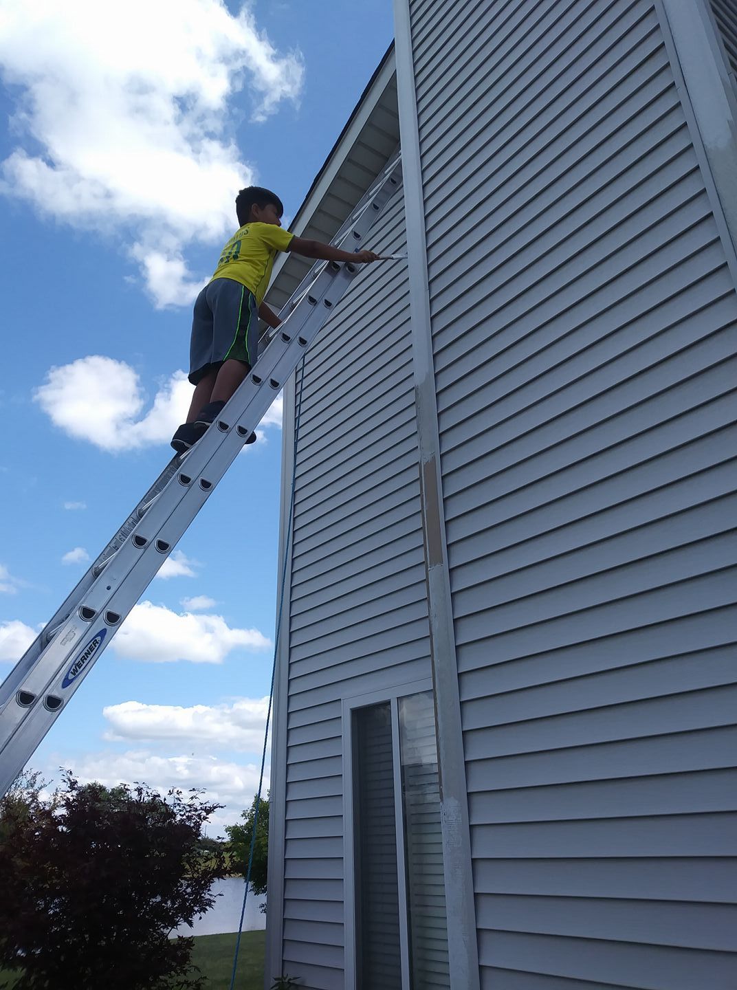 Person on a ladder cleaning the side of a house under a blue sky