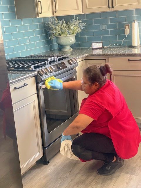 A woman in a red shirt is cleaning an oven in a kitchen.