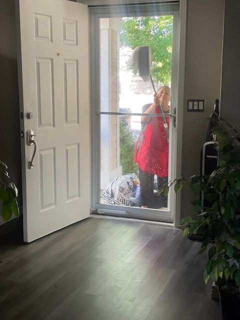 A woman is cleaning a window with a broom in a living room.