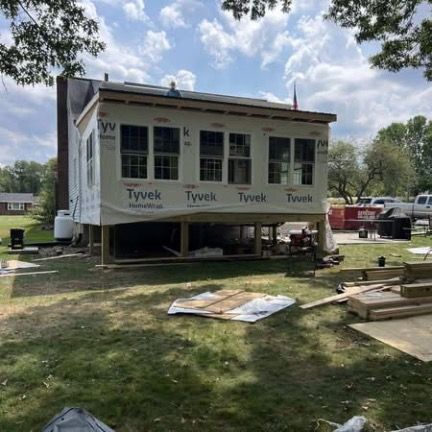 Construction of a wooden porch addition to a house; unfinished frame with a red ladder inside.