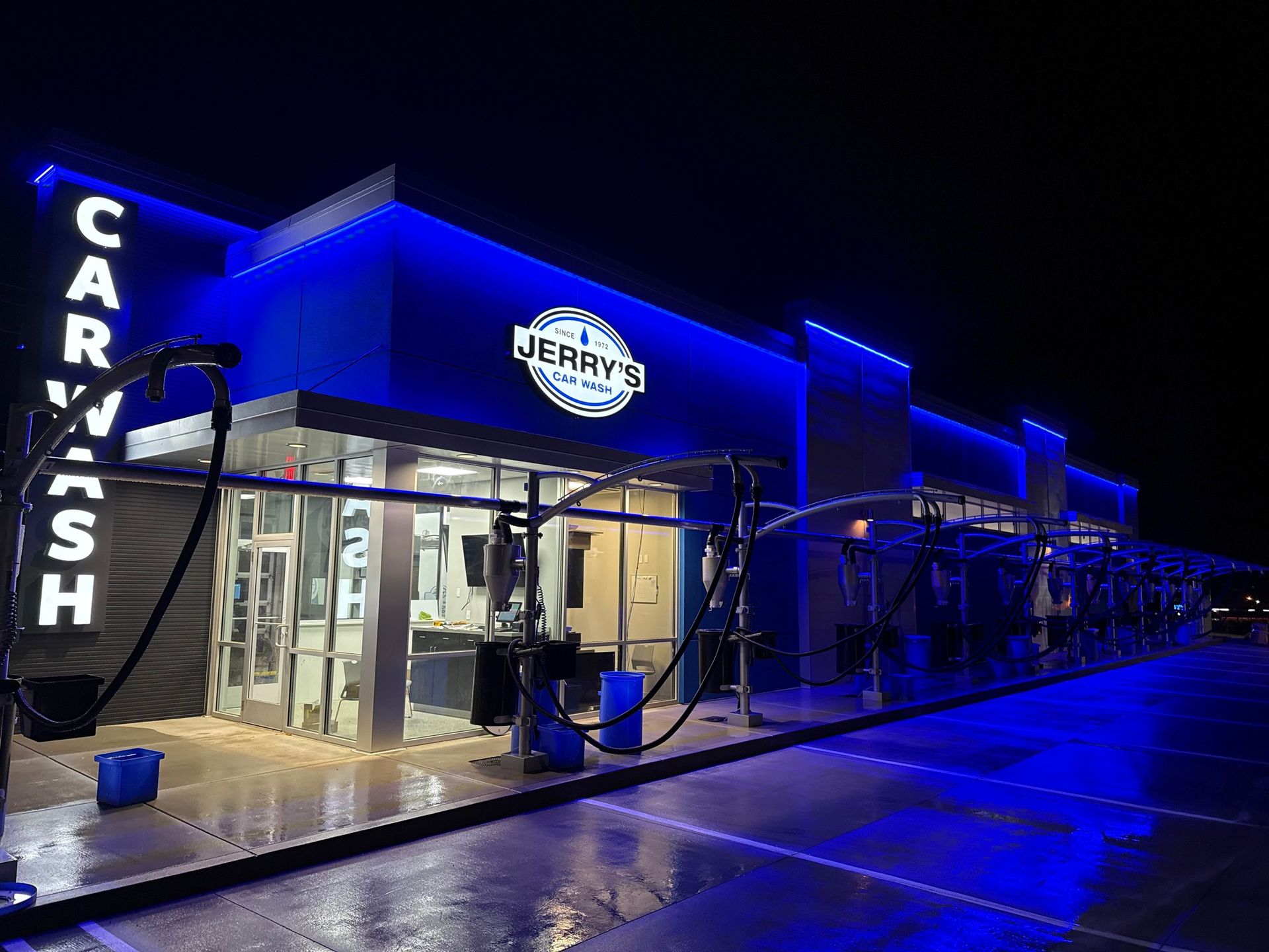 A car wash is lit up with blue lights at night.