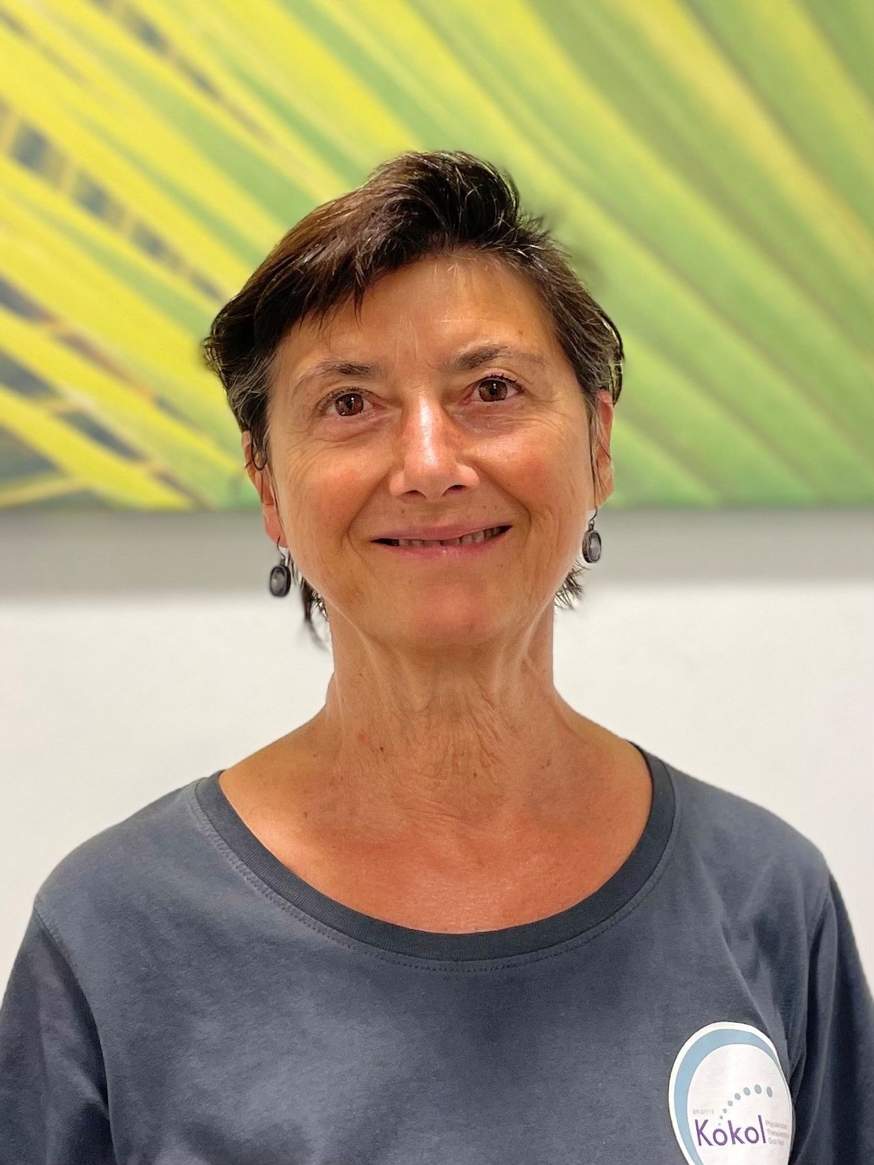 Eine Frau in einem grauen Hemd und Ohrringen lächelt in die Kamera.