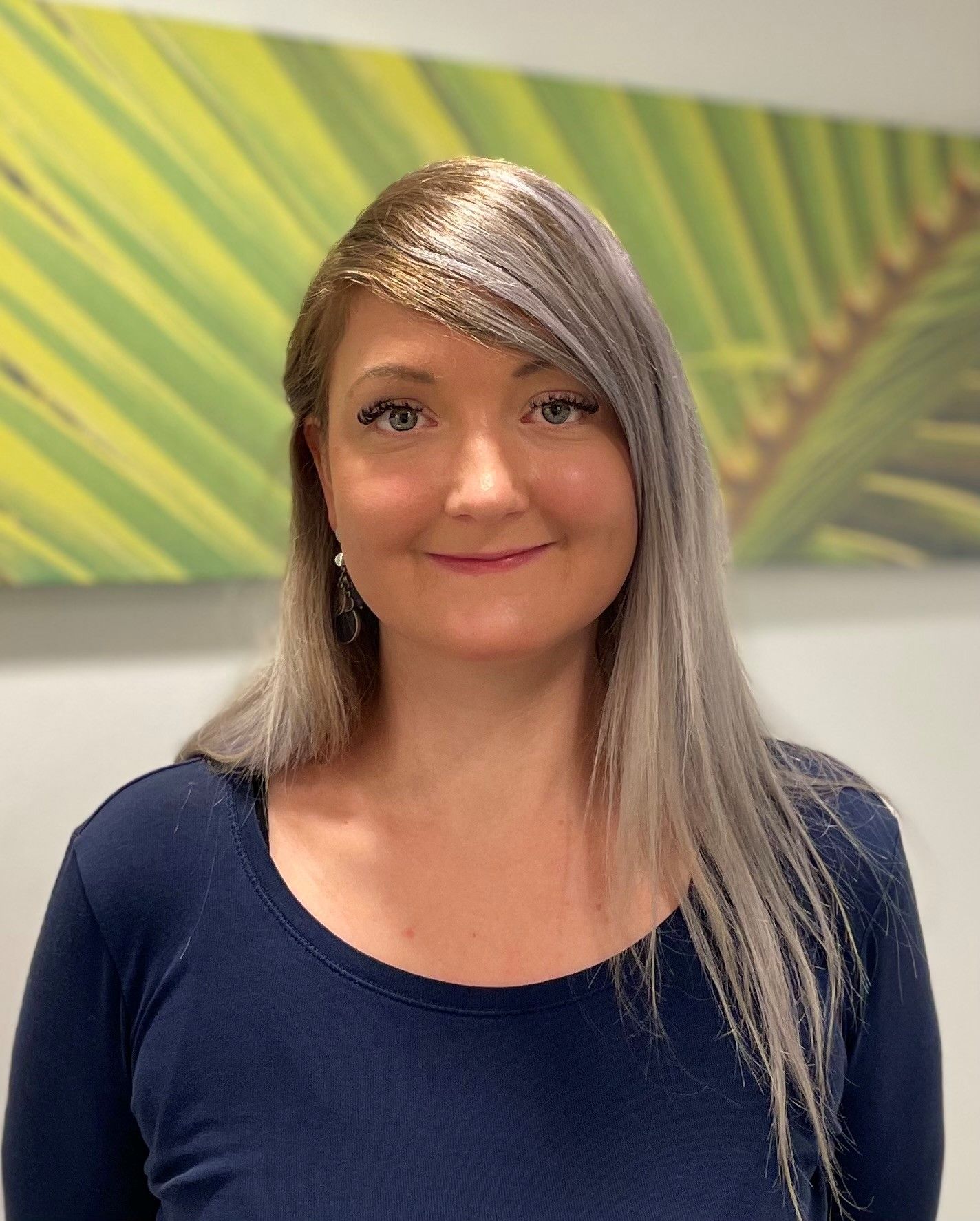 Eine Frau in einem blauen Hemd steht vor einem Gemälde mit Palmblättern.