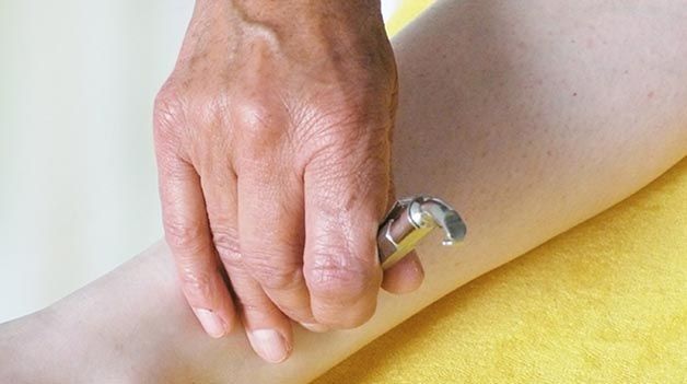 Eine Person hält einen Metallgegenstand am Arm einer anderen Person.