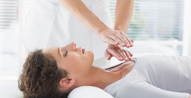 Eine Frau liegt auf einem Bett und bekommt eine Reiki-Behandlung.