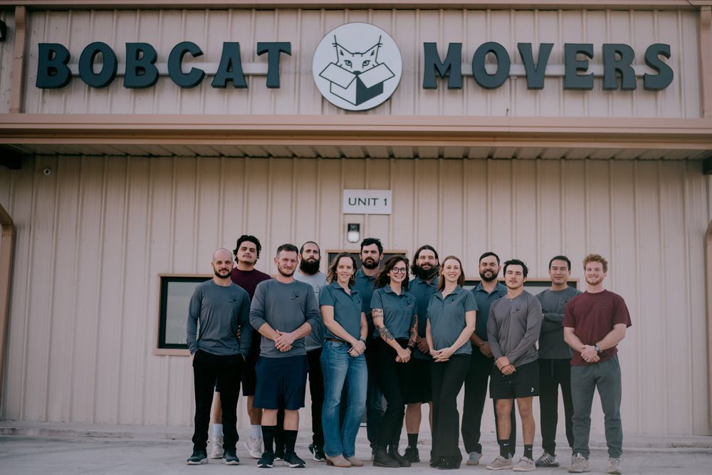 A group of people are posing for a picture in front of a bobcat movers building.