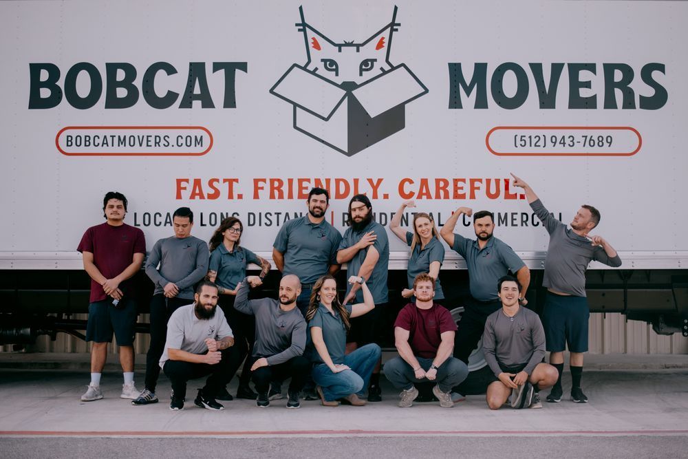 A group of people are posing for a picture in front of a bobcat movers truck.