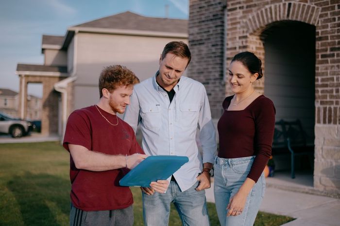 A man and two women are standing in front of a house looking at a clipboard.