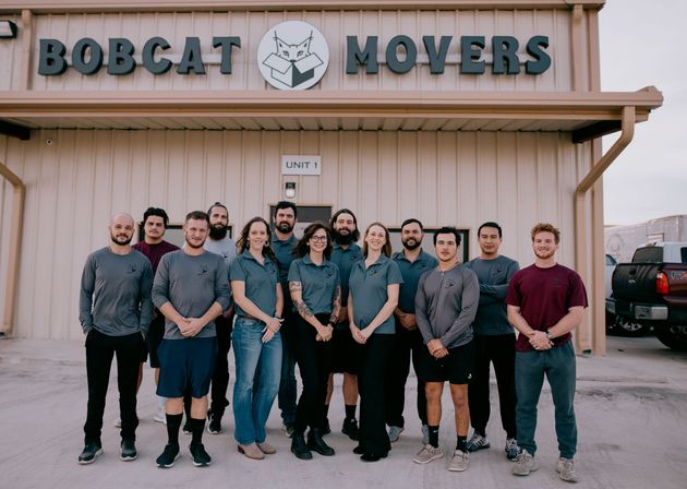 A group of people are posing for a picture in front of a bobcat movers building.