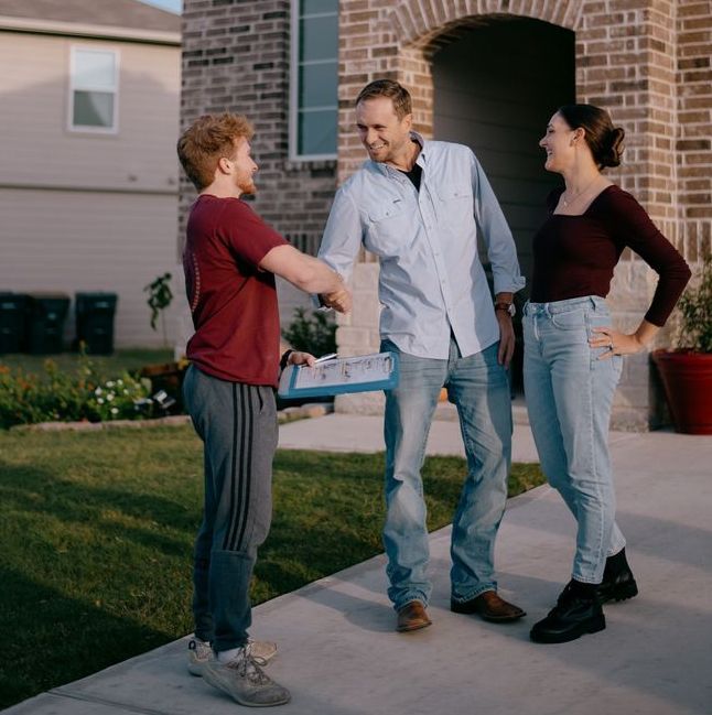 Three people are standing outside of a house talking to each other