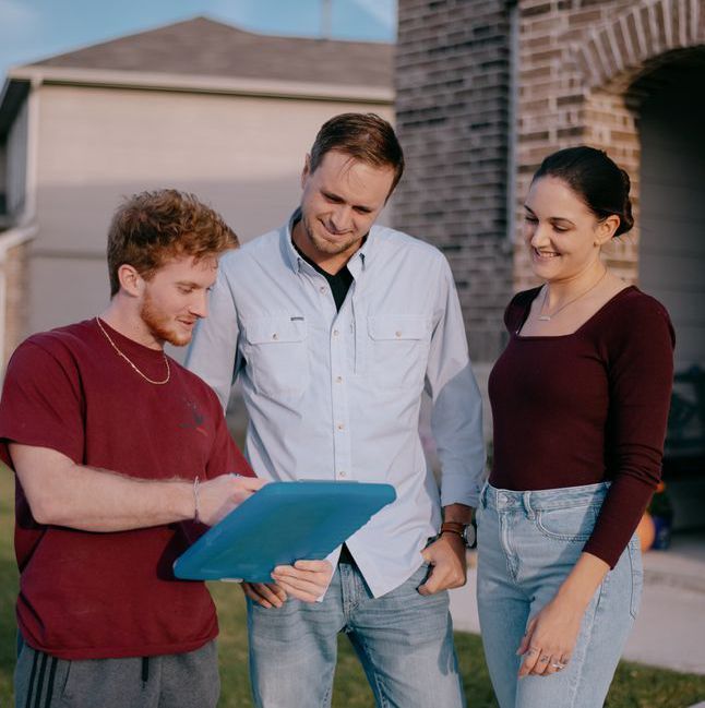 A group of people standing in front of a house looking at a tablet