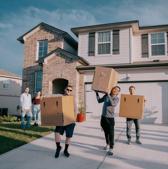 A group of people are carrying cardboard boxes in front of a house.
