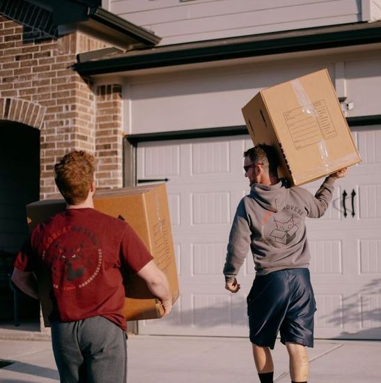 Two men are carrying cardboard boxes in front of a garage door