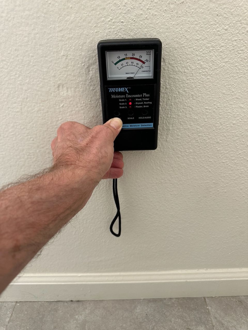 Person holds a moisture meter to a white wall, testing for dampness.