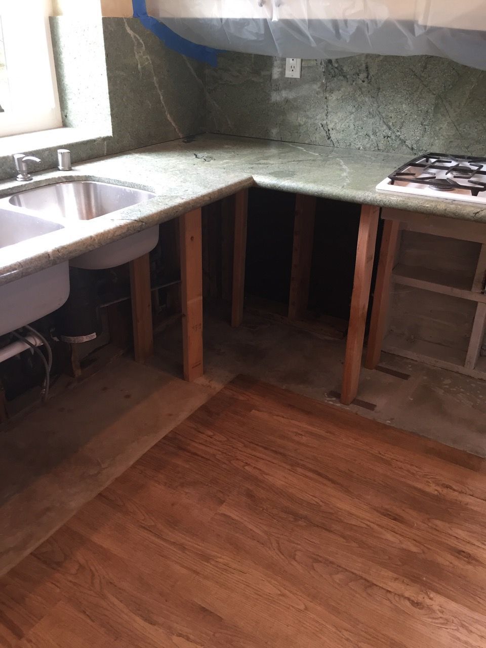 Kitchen under construction: granite countertops, exposed wood supports, sink, gas stovetop, hardwood floor.