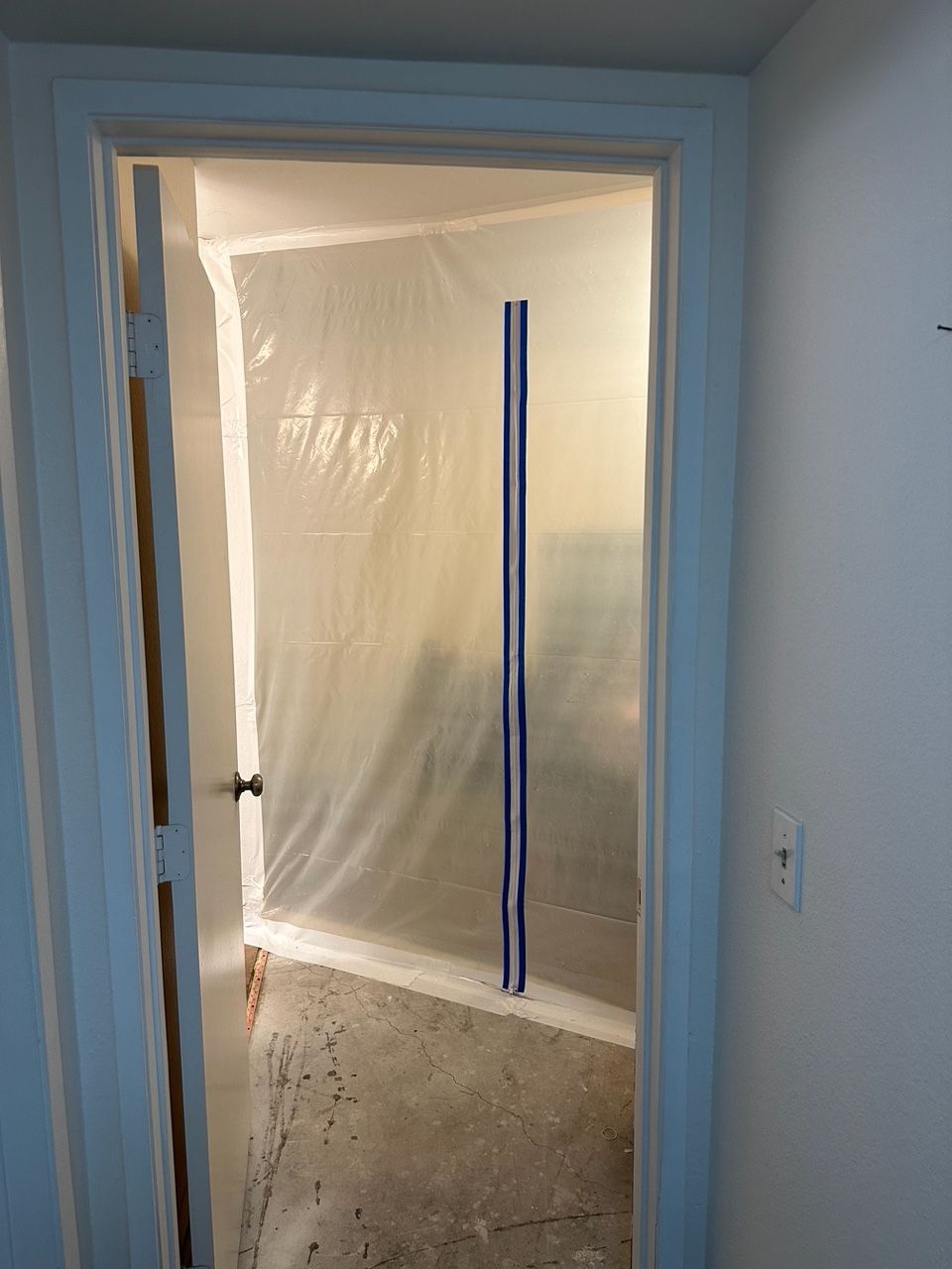 Doorway sealed with plastic sheeting for construction, with a vertical support bar.