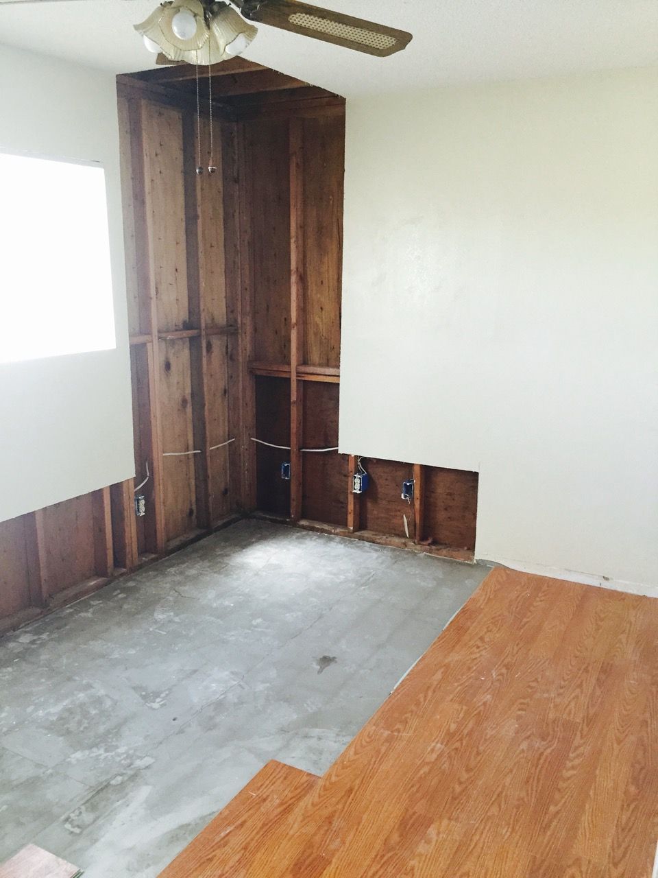 Interior room with exposed wooden studs, drywall removed. Brown wood, white walls, cement floor.