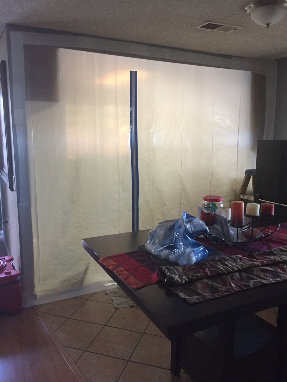 A translucent plastic barrier attached to a frame in a room, partially obscuring a table with items on it.