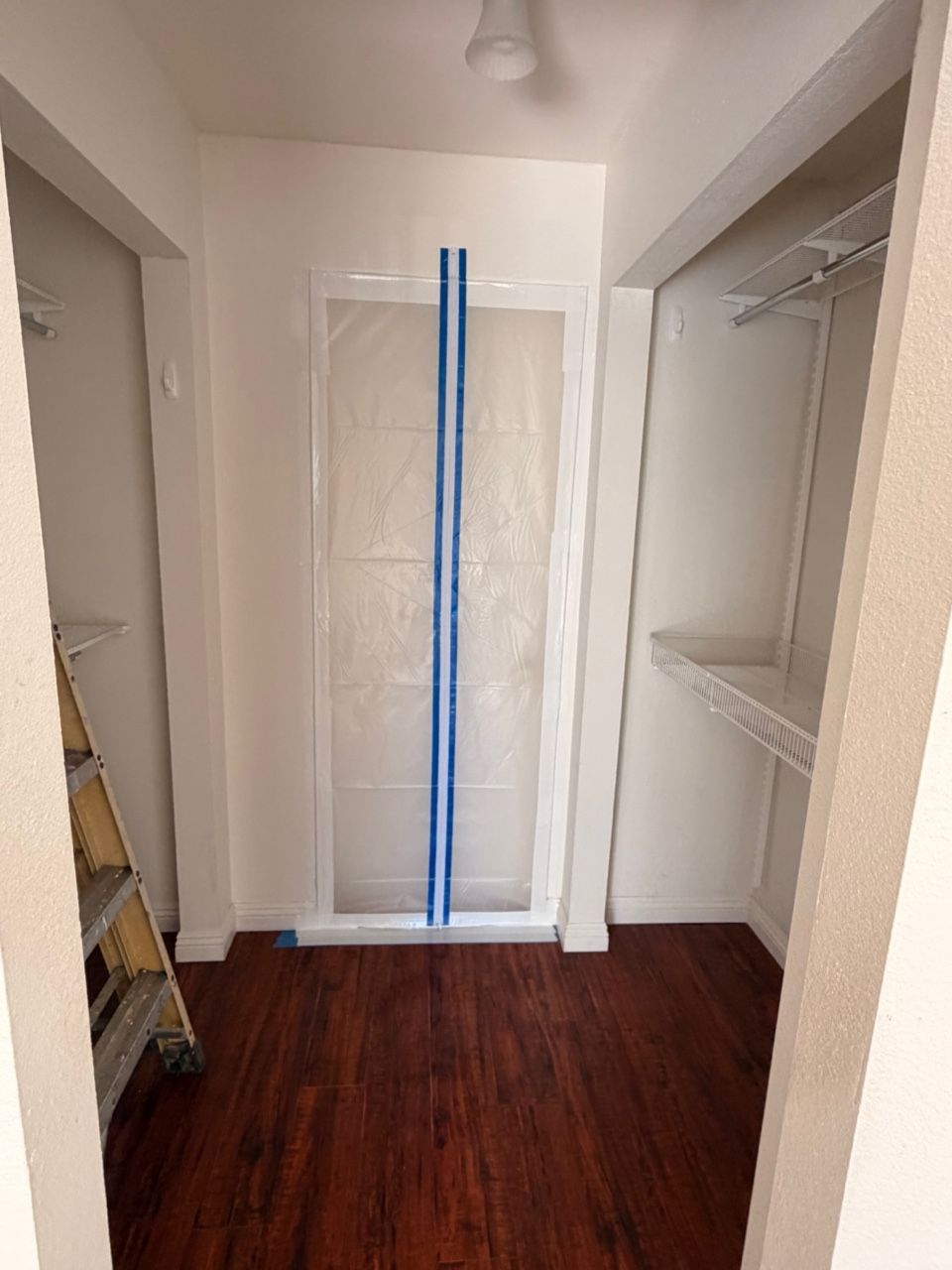 Narrow room with white walls, dark wood floor, and a framed glass door. A small ladder is to the left.