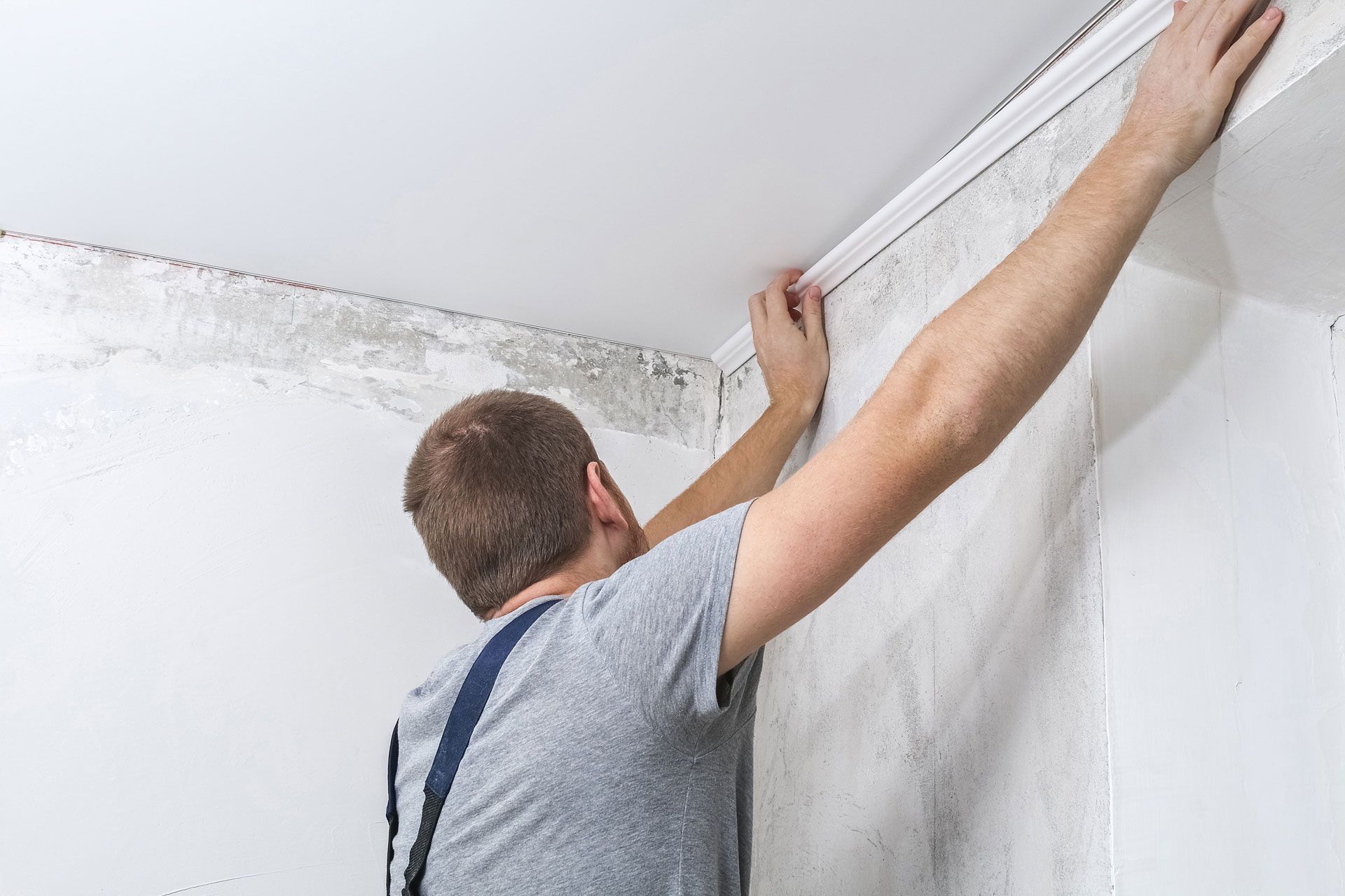 Person installing crown molding on a wall.