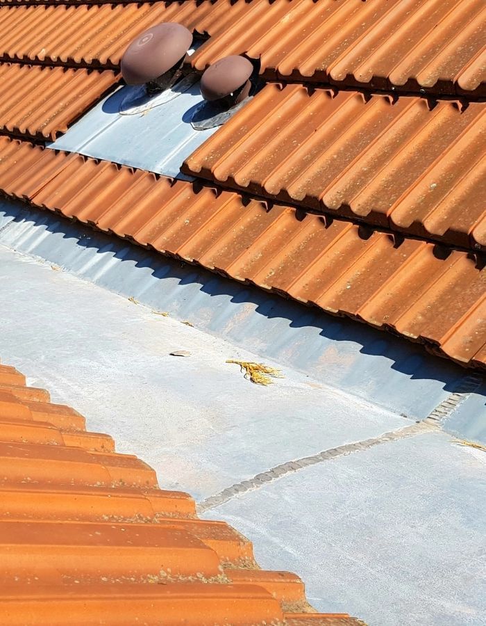 Orange tile roof with gray metal flashing and two brown vents.