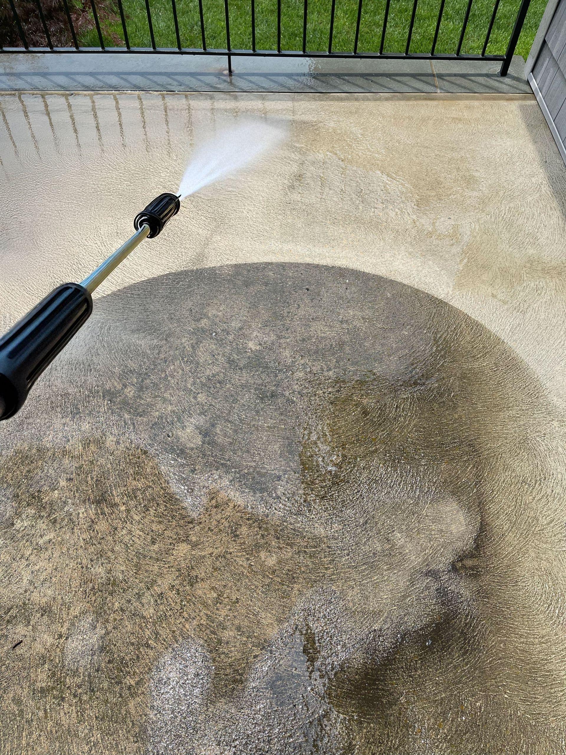 Man in white shirt, hat, pressure washing a driveway in front of a house, smiling.
