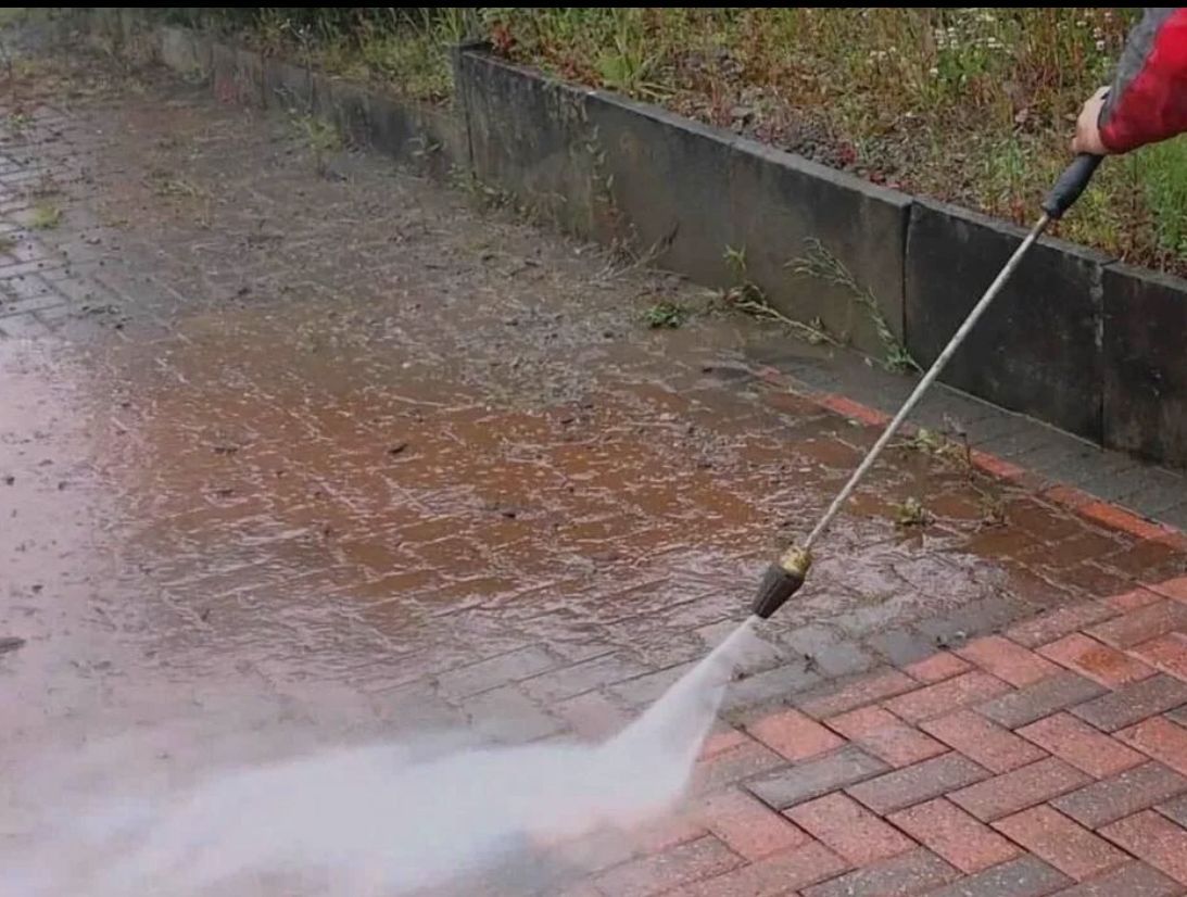 Man power washing a driveway in front of a brick house.