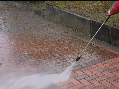 Man power washing a wet driveway in front of a brick house.
