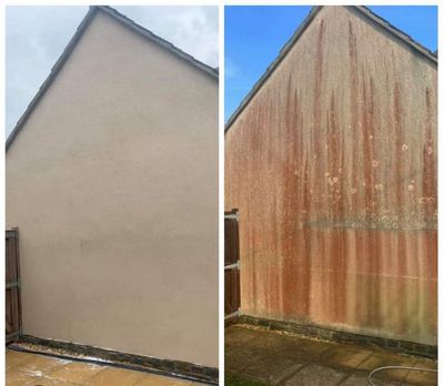 Man power washing the exterior of a beige house with green algae.