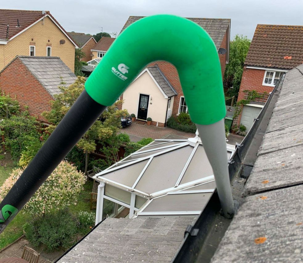Man cleaning gutters with a vacuum, standing in front of a brick house.