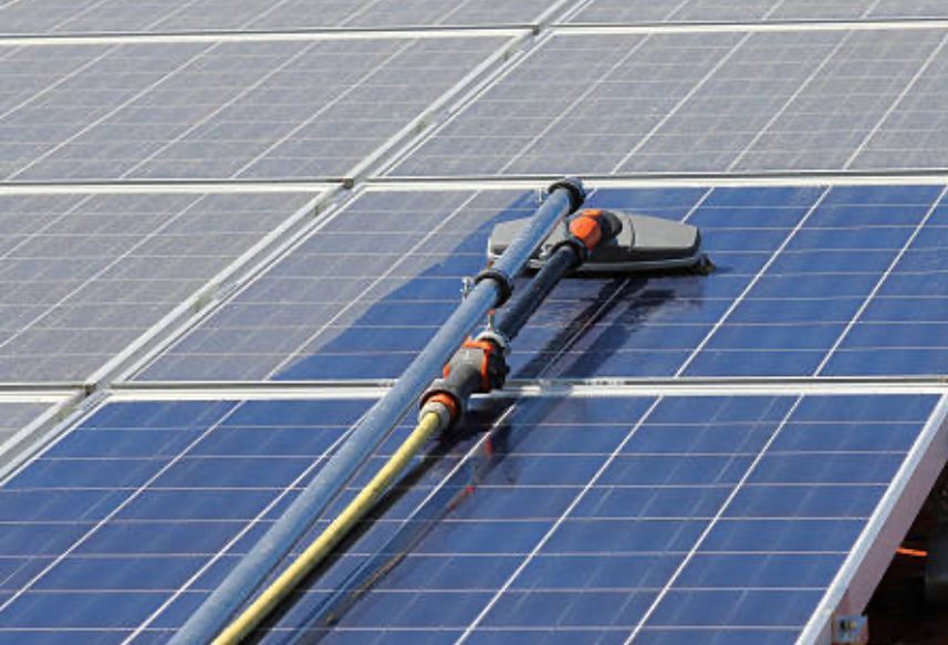 Man cleaning solar panels on a roof with a long-handled brush; house exterior.
