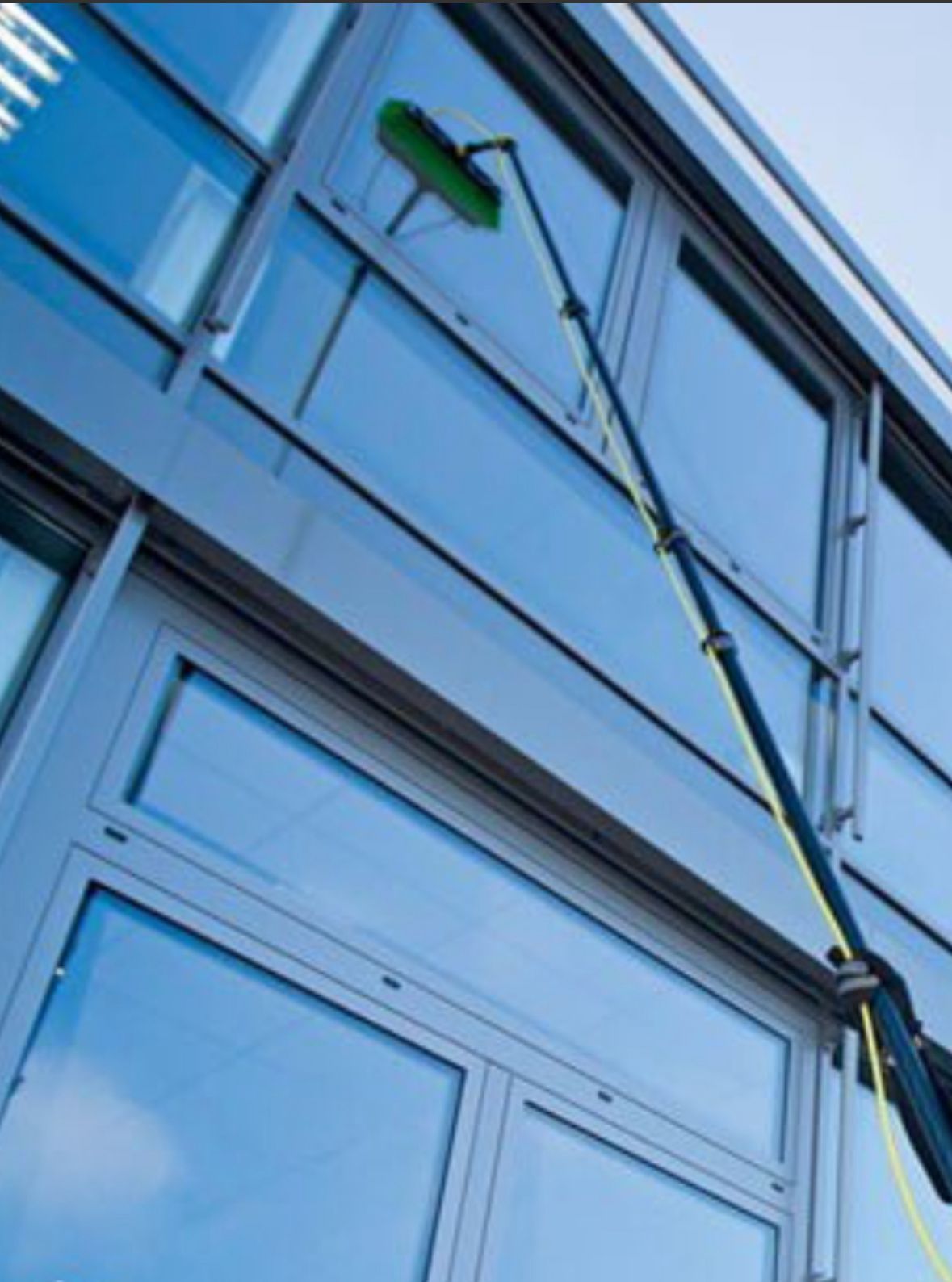 Man cleaning window of house with a long pole. DC Exteriors logo on shirt.
