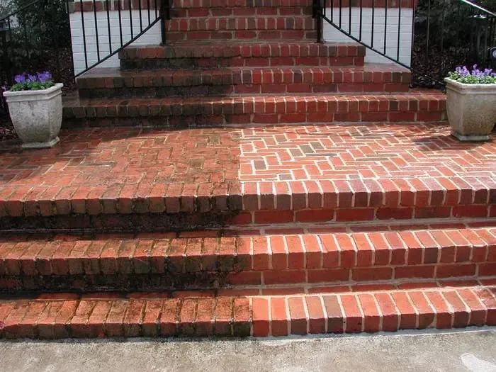 Brick steps and patio, half cleaned, showcasing the contrast of dirt and bright red brick.