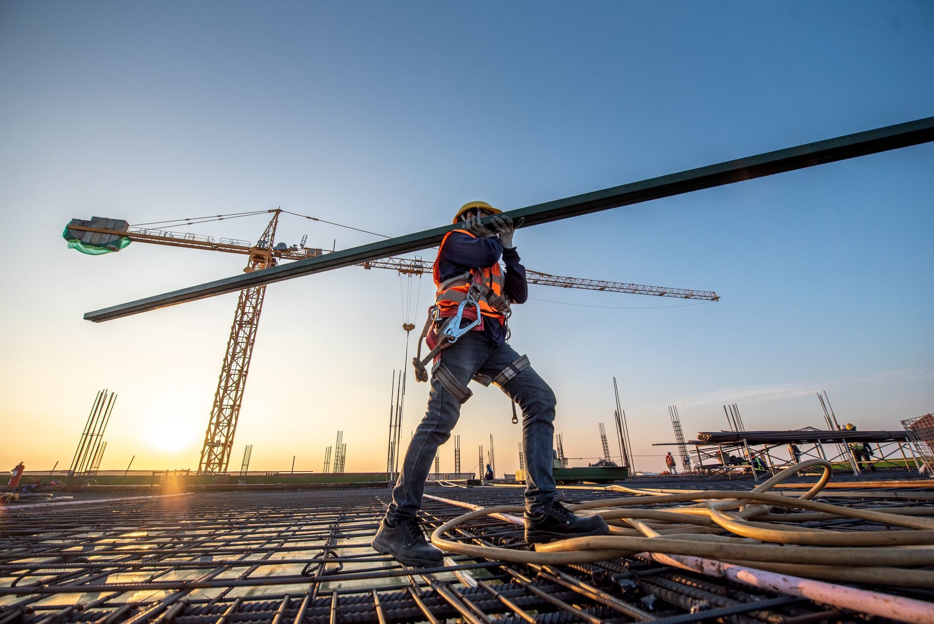 A construction worker is carrying a large pipe on his shoulder at a construction site.