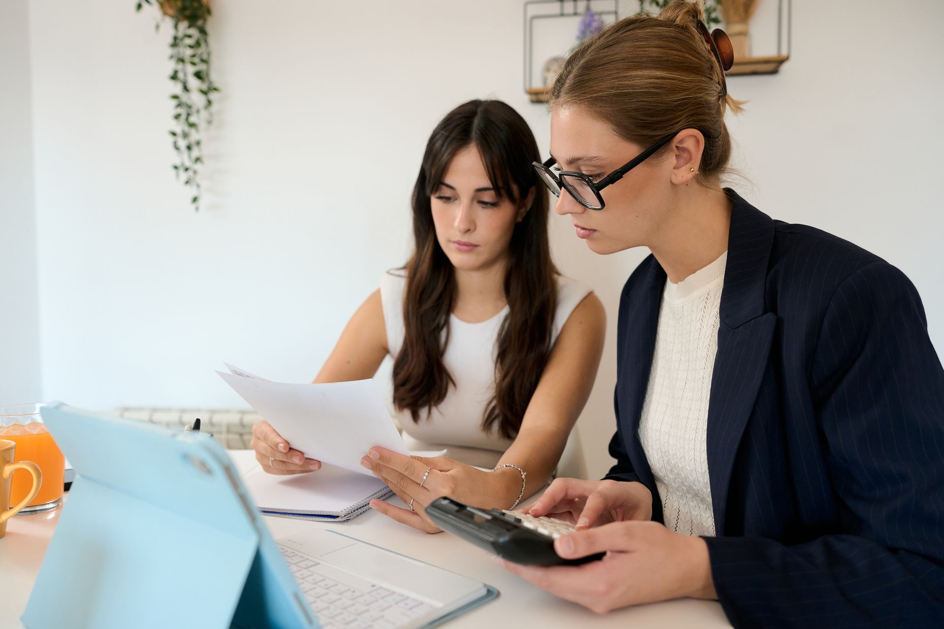 Two professionals reviewing financial documents with a calculator and laptop on a desk. Two professionals reviewing financial documents with a calculator and laptop on a desk.